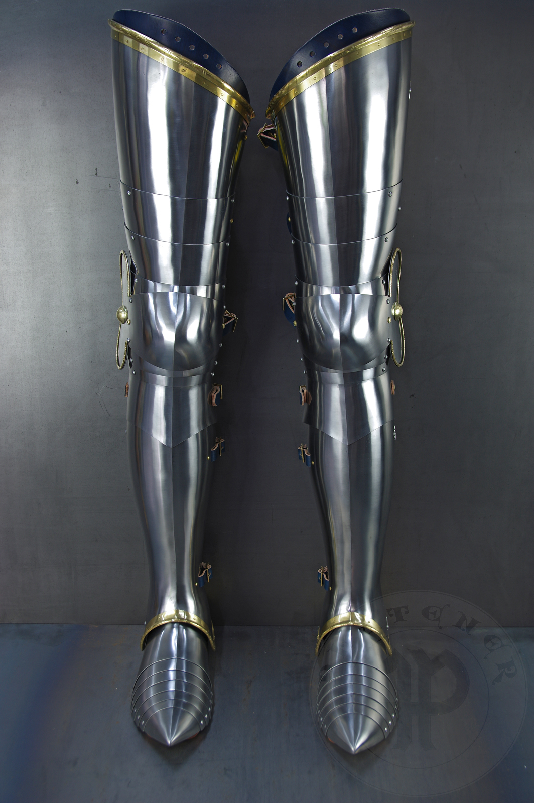 Late 14th/early 15th c. style full plate leg harness with brass decorations with a geometrical, hand filed pattern. Material: medium carbon and spring steel of various thickness: 1 mm; 1,2 mm and 1,5 mm; brass; vegetable tanned leather. Heat treatment: cuisses (thigh plates, lames, poleyns and demi-graves) heat hardened and tempered up to 42 HRC.